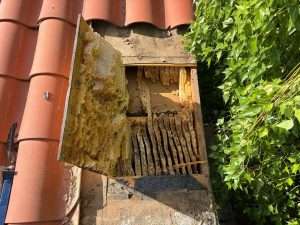 Roof deck cut open under lifted barrel tile to reach honeycomb in the rafter bay