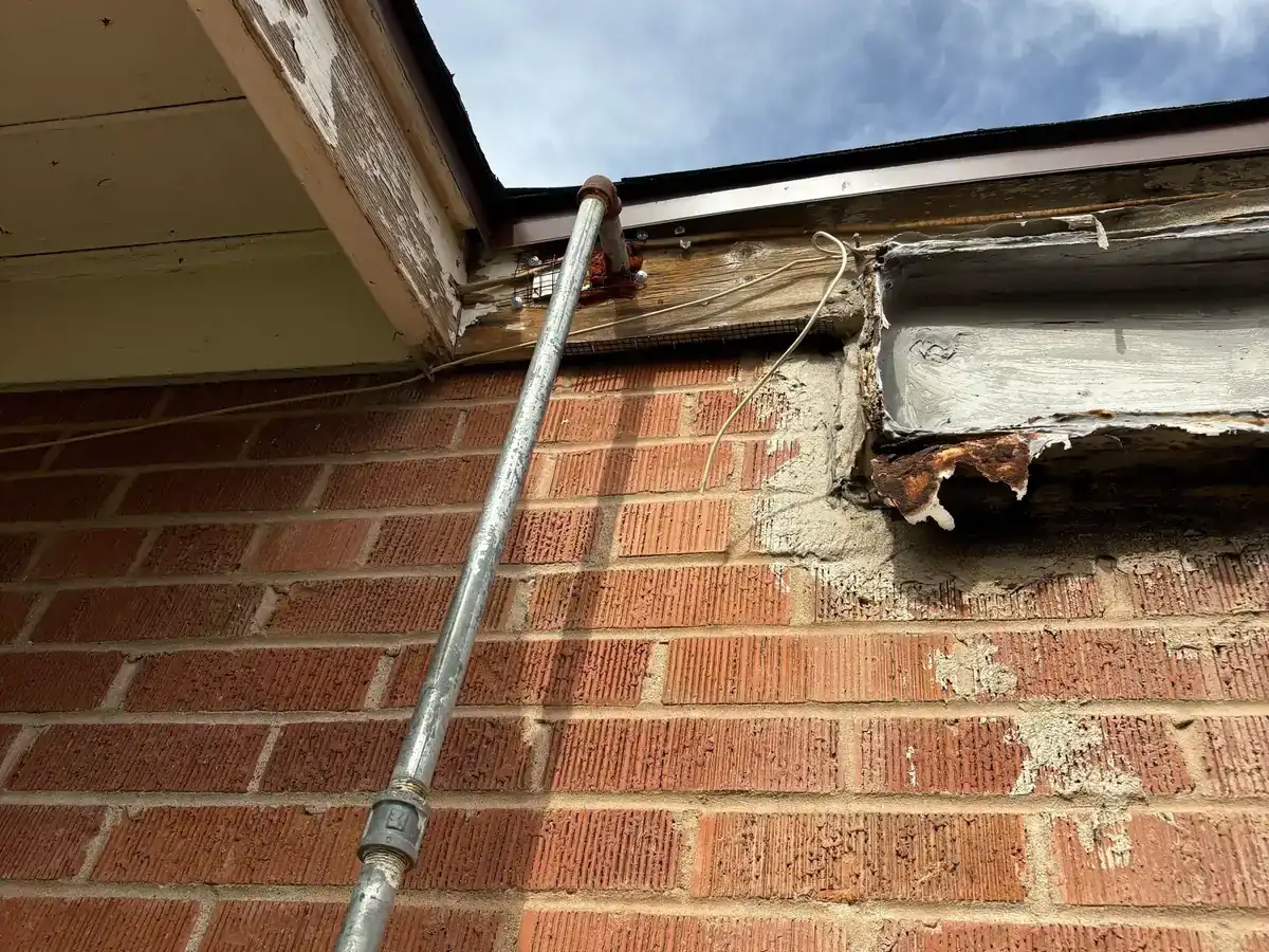A brick wall with damaged mortar and an open cavity beside a vertical pipe run