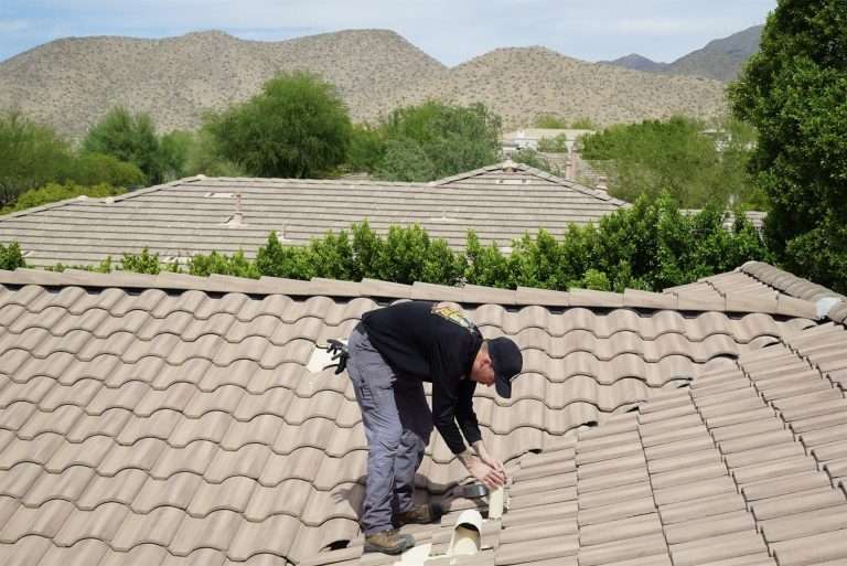 Technician screening a roof vent on a tile roof, with desert mountains behind the house